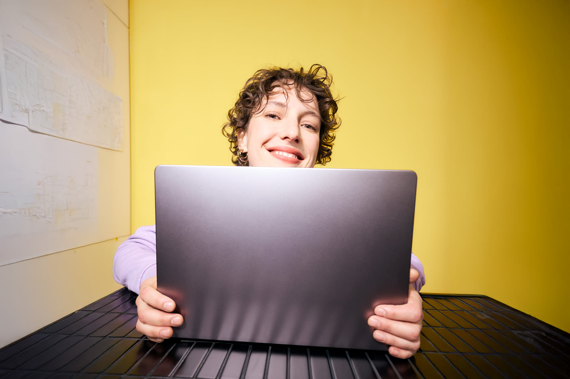 Mlada ženska dela na prenosnem računalniku pred rumenim ozadjem - fleksibilno vlaganje s prihranki pri banki BKS.