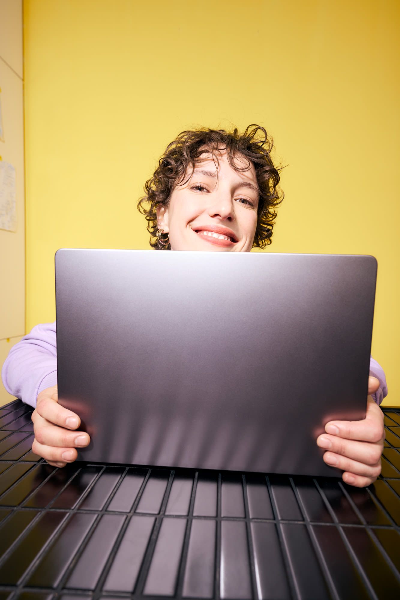 Mlada ženska dela na prenosnem računalniku pred rumenim ozadjem - fleksibilno vlaganje s prihranki pri banki BKS.