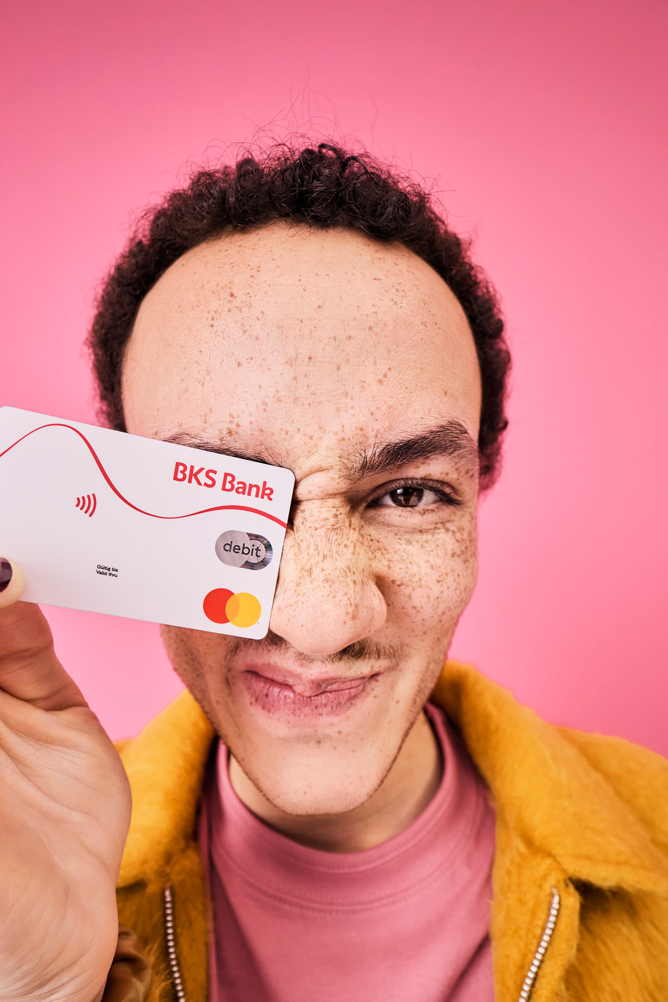 Muškarac drži BKS debitnu karticu ispred ružičaste pozadine – beskontaktno plaćanje s BKS Bankom.